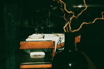 Restaurant window with sorted tables, white tablecloths, glasses behind window Black modern vase and twisted tree branches Natural decor in a dark key