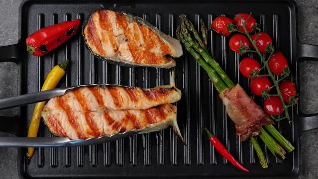 Salmon steak grill with vegetables on grill pan. Salmon steak turning over on the grill. Top view. Slow motion