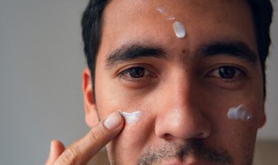 latin man applying moisturizer on his face