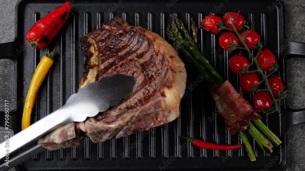 Wall mural T- bone beef steak grill with vegetables on grill pan. Steak turning over on the grill. Top view. Slow motion