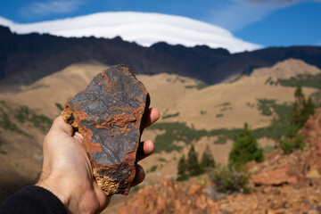 Holding a volcanic rock with a mountain landscape in the background in Patagonia