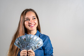 Mujer feliz y sonriente sosteniendo mucho dinero en forma de abanico y mirando hacia arriba en actitud soñadora