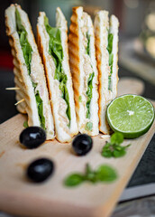 two sandwiches with tuna and lettuce, black olives, and lime on a wooden cutting board