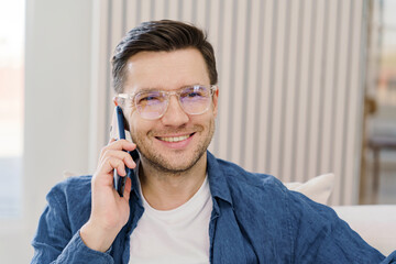 Affable professional in a smart-casual ensemble converses on a smartphone in a modern, well-lit interior.