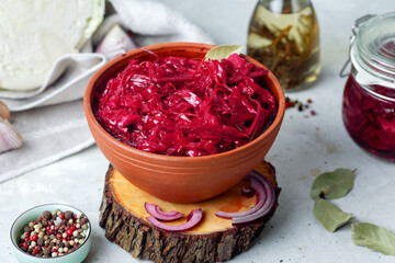 Fermented vegetables cabbage with carrot and beetroot in clay bowl with spices, grey background.
