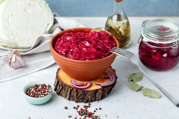 Fermented vegetables cabbage with carrot and beetroot in clay bowl with spices, grey background.