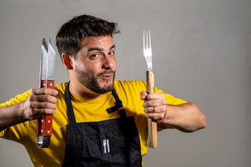 Hombre cocinero feliz y entusiasmado sosteniendo sus utensillos de cocina. Fotografia de estudio con fondo blanco