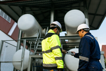 Two men wearing safety gear and holding a laptop, looking at something on the screen. Scene is serious and focused