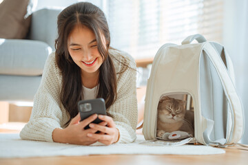 Happy asian woman using her mobile phone while a cat sleeping peacefully in her cat bag, Happy...