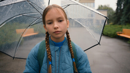 Tired little girl schoolgirl child looking at camera bored unhappy bad weather rain umbrella city...