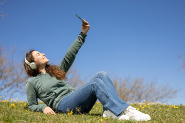 smiling girl taking a selfie lying on the meadow while listening to music on her headphones