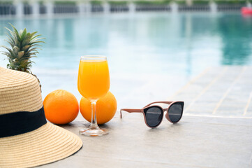Time to relax on a summer day. Summer mood. Leisure at the pool. Fresh orange juice, hat, pineapples, and sunglasses near the swimming pool.