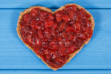 Bread in shape of heart with strawberry jam for breakfast. Blue boards background