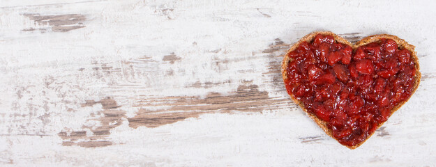 Bread in shape of heart with strawberry jam for breakfast. Place for text on rustic background