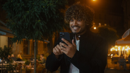 Indian Arabian Latino American man holding smartphone mobile phone cellphone telephone looking at...