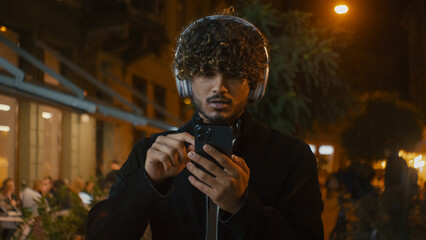 Indian Latino Arabian man in headphones using mobile phone smartphone cellphone listen music walk...