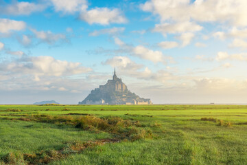 Mont Saint Michel abbey on the island with green meadow at sunrise, Normandy, Northern France, Europe. Tidal island with medieval gothic cathedral in Normandie. Travel and touristic destination