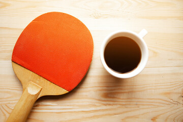 Ping pong racket and coffee cup on wooden background. Stay home concept
