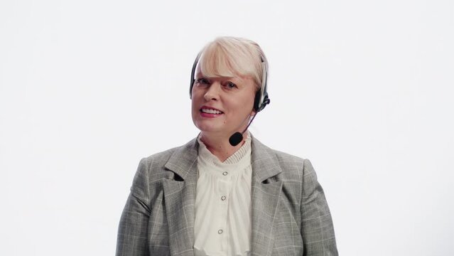 Portrait of a smiling mature caucasian woman in a headset, standing on a white background and talking with a client during a support service session