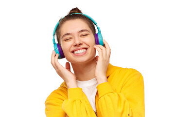 Young smiling teenage girl dressed in yellow hoodie, enjoying favorite music through wireless headphones with eyes closed