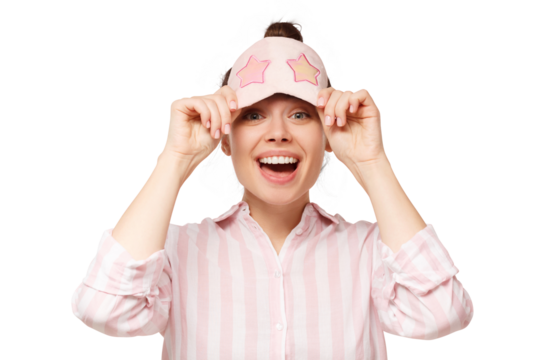 Young excited laughing woman holding pink sleeping mask on forehead and looking from under it, having fun on pyjama party