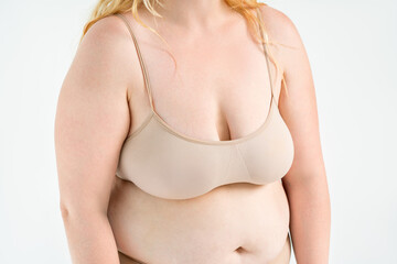 Large natural saggy breasts with asymmetry after breastfeeding in a beige top bra, big boobs on gray background, augmentation and plastic surgery concept