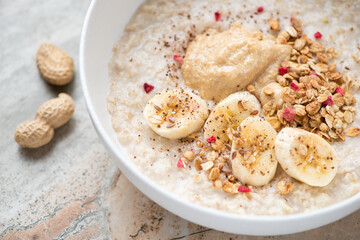 Oatmeal porridge served with peanut butter, fresh banana and granola in a white bowl, close-up,...