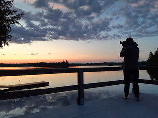 Silhouette of photographer at sunset taking a picture of a Canadian lake. 