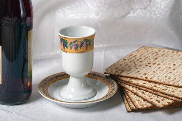 Wine bottle, an ornate goblet, and matzah bread against a white lace backdrop. The matzah is crisp, browned, and patterned with holes. Pesah celebration, Jewish Passover holiday with passover seder