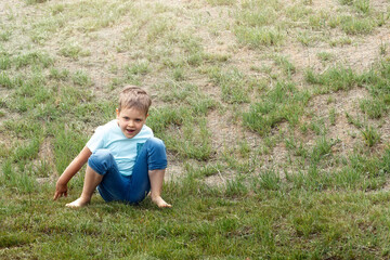 A cute six-year-old boy comes down from the mound and sits on a of dry grass