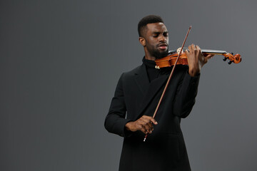 Professional African American male violinist in elegant black suit performing solo on gray background