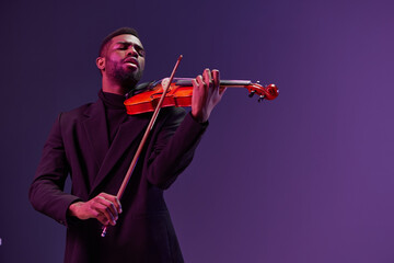 Elegant musician in black suit playing violin on vibrant purple background with passion and skill