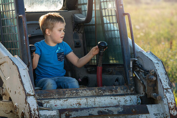 A cute little boy is playing with a tractor and trying to control it