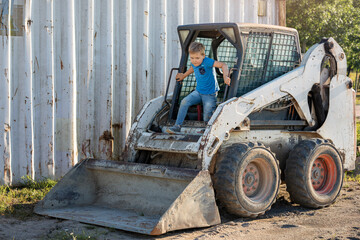 A little old bobcat backhoe in the yard by the garage and a little boy playing in it