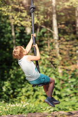 A little boy from back is rolling down a tightrope in a beautiful evening sun summer forest