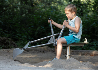A cute boy is learning and trying hard to dig sand by controlling the manipulators of the excavator