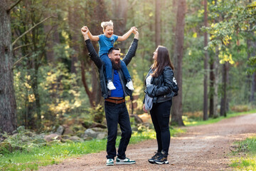Happy emotion and facial expression of father and son, they amuse mom by joking. A happy family walking along a forest path on a summer evening