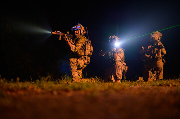 Obraz premium Soldiers in camouflage uniforms aiming with their rifles.ready to fire during Military Operation at night, soldiers training in a military operation
