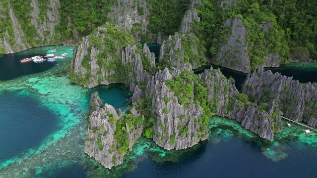 Aerial around view of tropical island. Boats in blue lagoons, rocks cliffs mountains and coral reef, Philippines, 4k