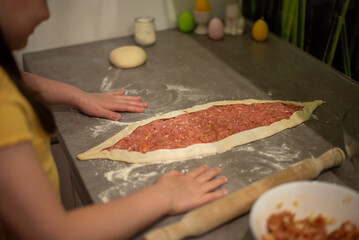 A child prepares pide, Turkish pizza. A girl rolls out dough to make a meat pie.