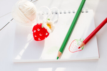 A knitted strawberry is lying on the album. Painted berry with pencils, handmade