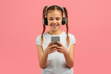 Teen girl with headphones using smartphone on pink background