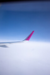 A pink and white aircraft wing soars through the cloudy sky