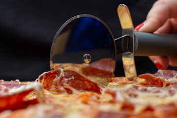 Slicing salami pizza with a round pizza cutter