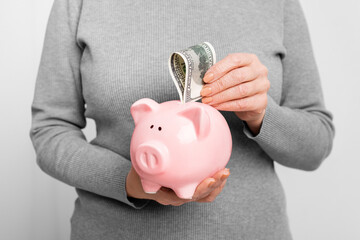 Elderly woman saving money in a pink piggy bank