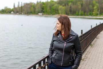 a woman in a black leather jacket is standing on a bridge overlooking a lake