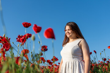 A woman in a white dress smiles among red flowers in a field