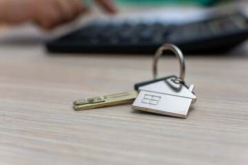 Metal keys with house keychain on wood table near calculator