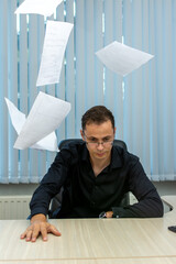 a man sitting at a desk with papers falling around him