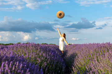 Cute woman in lavender field throwing hat at the sky